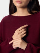 Close-up of a woman wearing a deep burgundy knit sweater with a wide boat neckline and long sleeves, with her hands crossed over her chest.