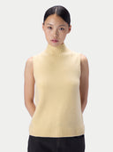 A model wearing a pale yellow knit sleeveless turtleneck sweater vest against a light gray studio background.