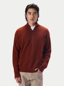 A man wearing a rust-brown quarter-zip knit sweater over a white undershirt and beige trousers, standing against a light gray studio background.#color_coconut-brown
