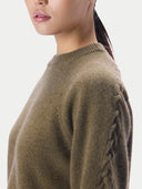 Close-up side view of a woman wearing a soft knit sweater in a muted olive-brown color, showing the side neckline and textured sleeve detail against a plain light background.