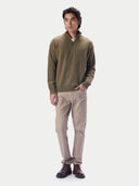 A man modeling a half-zip knit sweater in olive green, paired with beige trousers and dark brown leather shoes, against a light gray studio background.