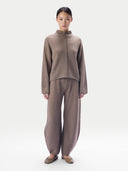front view of a woman standing wearing a taupe outfit, (sweater, wide leg pants)