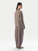 A model shown from the back wearing a matching taupe knit sweater and wide-leg trousers set, paired with flat taupe shoes, against a plain light gray studio background.
