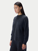 A woman wearing a dark charcoal gray knit sweater and matching dark pants, shown in profile against a light gray studio background.