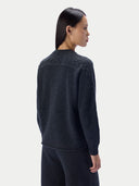 A woman shown from the back wearing a dark charcoal gray knit sweater and matching dark pants against a light gray studio background.