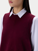 A close-up of a model wearing a burgundy knit sweater vest over a white collared shirt, cropped from the lower face to the upper torso against a plain light background.