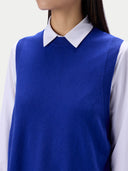 A close-up of a person wearing a royal blue knit sweater vest over a white collared shirt, cropped from the lower face to the upper torso against a plain light background.