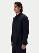 Side profile of a man wearing the black cashmere stand-collar jacket against a light gray studio background.