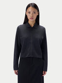 A model wearing a dark charcoal gray long-sleeve knit polo-style top with a front zipper, paired with a black skirt, against a light gray studio background.
