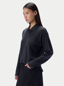 A woman wearing a dark charcoal gray knit polo-style top with long sleeves and a collar, paired with a dark skirt, photographed against a clean light gray studio background.