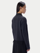A model shown from the back wearing a dark charcoal gray mock neck knit sweater and a black skirt, set against a plain light gray studio background.