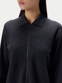 A close-up of a model wearing a dark charcoal gray zip-up knit sweater with a collar, shown from the chest up against a light gray background.