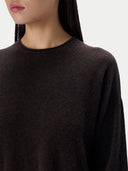 Close-up of a person wearing a dark brown crew-neck knit sweater against a plain light background.