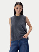 A model wearing a dark gray sleeveless knit top and blue jeans, standing against a light gray studio background.