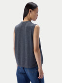 A woman shown from the back wearing a dark gray sleeveless knit top and blue jeans against a light gray studio background.