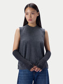 A woman modeling a dark gray sleeveless mock-neck knit top with ribbed knit arm warmers, paired with blue jeans, against a light gray studio background.
