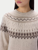 A close-up of a woman wearing a cream-colored knit sweater with brown and gray Fair Isle patterns across the chest and shoulders.