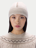 A woman wearing a light beige ribbed knit beanie and a matching beige knit sweater with a brown zigzag pattern, shown against a plain light gray background.