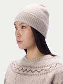A woman wearing a light beige ribbed knit beanie hat and a matching beige patterned knit sweater, shown in a side profile against a plain light gray background.