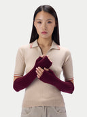 A model wearing a pair of dark burgundy ribbed fingerless arm warmers over a beige ribbed polo sweater with thin red stripes on the collar and sleeves, set against a plain light gray background.