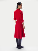 A model shown from the back wearing a bright red mock-neck midi dress with three-quarter sleeves, paired with dark gray boots, against a light gray studio background.