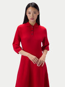 A woman modeling a bright red long-sleeve polo dress with a three-button placket, photographed against a clean light gray studio background.