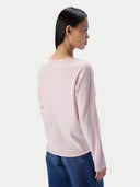 A woman shown from the back wearing a light pink long-sleeve knit top and blue jeans against a plain light gray studio background. _delicate-pink