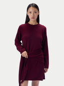 A woman modeling a long-sleeve knit wrap dress in deep burgundy against a plain light gray studio background.