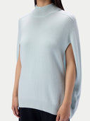 A woman wearing a pale icy blue knit mock-neck sweater with side slits, shown from the neck down against a light gray studio background.