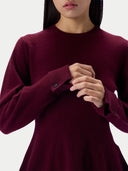 A close-up of a model wearing a long-sleeve crewneck sweater in deep burgundy, showing the fabric texture and buttoned cuffs.