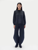 A model stands against a light gray studio background wearing a dark charcoal gray knit sweater and matching wide-leg knit pants with black shoes.