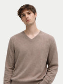 A man wearing a light brown v-neck knit sweater, photographed against a plain light gray studio background.