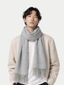 Man wearing a beige sweater, white shirt, black pants, and gray scarf on a white background