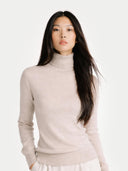 A light beige knit cashmere turtleneck sweater with long sleeves and ribbed cuffs and hem, displayed against a clean white background. #color_soft-beige