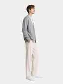 Man wearing a gray cardigan, white shirt, and white pants on a light gray background