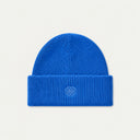 A ribbed knit beanie hat in a light beige or cream color, featuring a small tonal embroidered geometric logo on the front of the folded cuff, set against a solid off-white background.