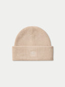 A beige ribbed knit beanie hat with a folded cuff, featuring a subtle tonal embroidered logo on the front, set against a light gray background.