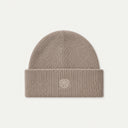 A ribbed knit beanie hat in a light beige or cream color, featuring a small tonal embroidered geometric logo on the front of the folded cuff, set against a solid off-white background.