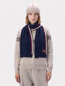 A model wearing the navy cashmere scarf around the neck over a cream Fair Isle sweater, with a beige beanie and light trousers.