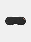The charcoal cashmere fine-knit eye mask with a small leather logo tab, laid flat against a light gray background.