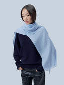 Model wearing the Muted Blue woven scarf draped around the neck over a navy sweater, front view
