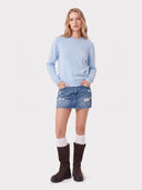 Model wearing the Seamless Cashmere Clean Crewneck Sweater in Soft Blue with a denim mini skirt and brown boots, full-length front view