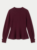 A long-sleeve crewneck knit top in deep burgundy, featuring a flared peplum-like hem and buttoned cuffs, displayed on a light gray background.