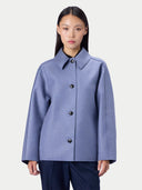 A model wearing a light periwinkle blue wool-blend jacket with a pointed collar and dark buttons, paired with dark trousers, against a light gray studio background.