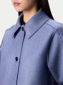 Close-up of a person wearing a blue-gray collared coat or jacket with dark buttons, cropped from the lower face to the upper torso against a light neutral background.