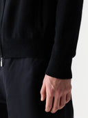 Person wearing a black sweater and dark pants on a white background
