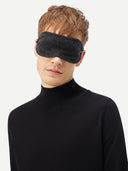 A man wearing the charcoal cashmere eye mask with a black turtleneck, head tilted.