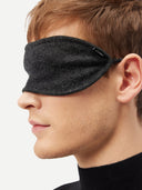 Side close-up of a man wearing the charcoal cashmere eye mask, showing the logo tab at the temple.