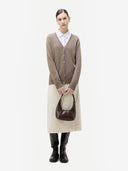 Person wearing a brown cardigan, white shirt, beige skirt, and black boots holding a brown handbag on a white background