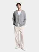 Man wearing a gray cardigan, white shirt, beige pants, and white sneakers on a white background